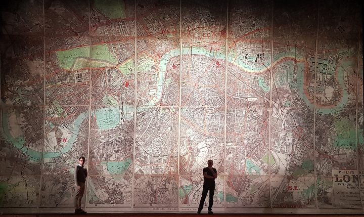 Two people standing in front of a detailed map of London which is used as backdrop